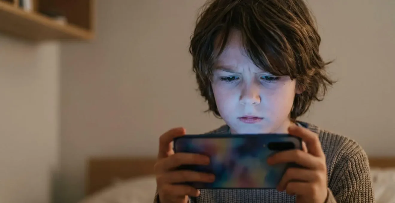 Child looking at glowing smartphone screen in dimly lit room showing concentration and digital engagement