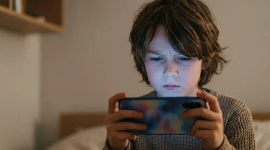 Child looking at glowing smartphone screen in dimly lit room showing concentration and digital engagement